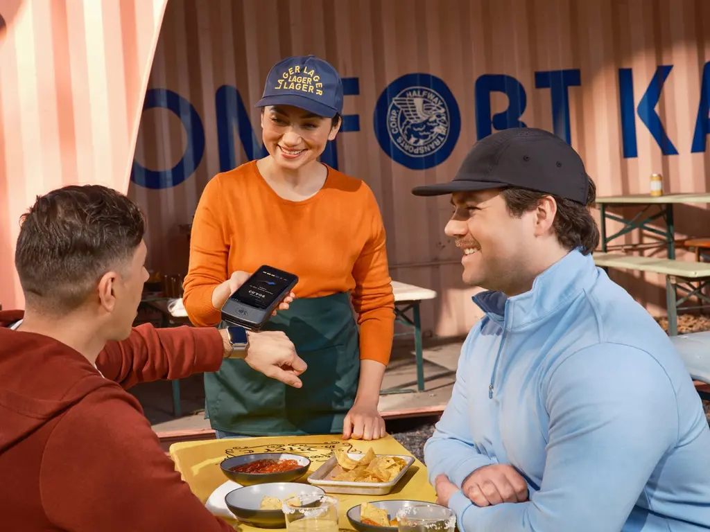 A café owner holding out a phone at the counter for a customer
